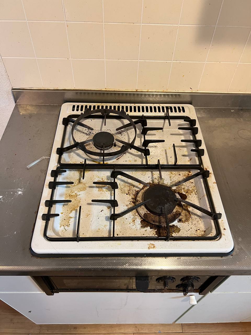 ガスコンロの五徳と天板に焦げ付き・油汚れ・こびりついた汚れが広がっている清掃前の状態｜おそうじフレッシュ