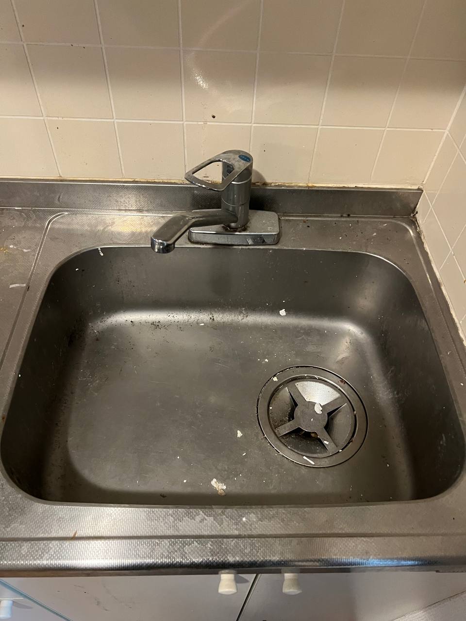 ステンレスシンク全体に油汚れ・水垢・白い固着汚れが広がり、排水口まわりもくすんでいる清掃前の状態｜おそうじフレッシュ