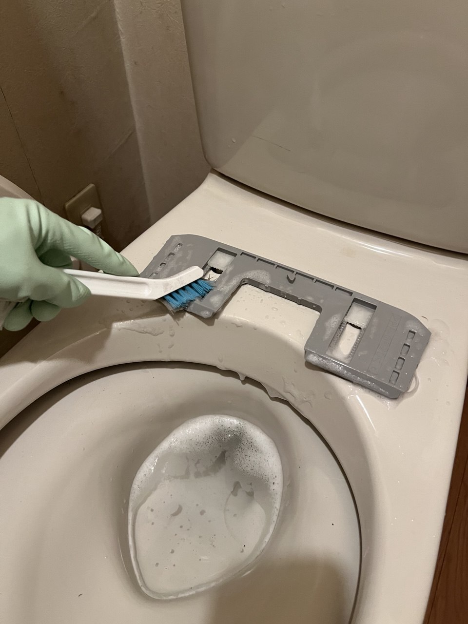 空室クリーニング中のトイレ便座取り外し金具部分の手作業洗浄